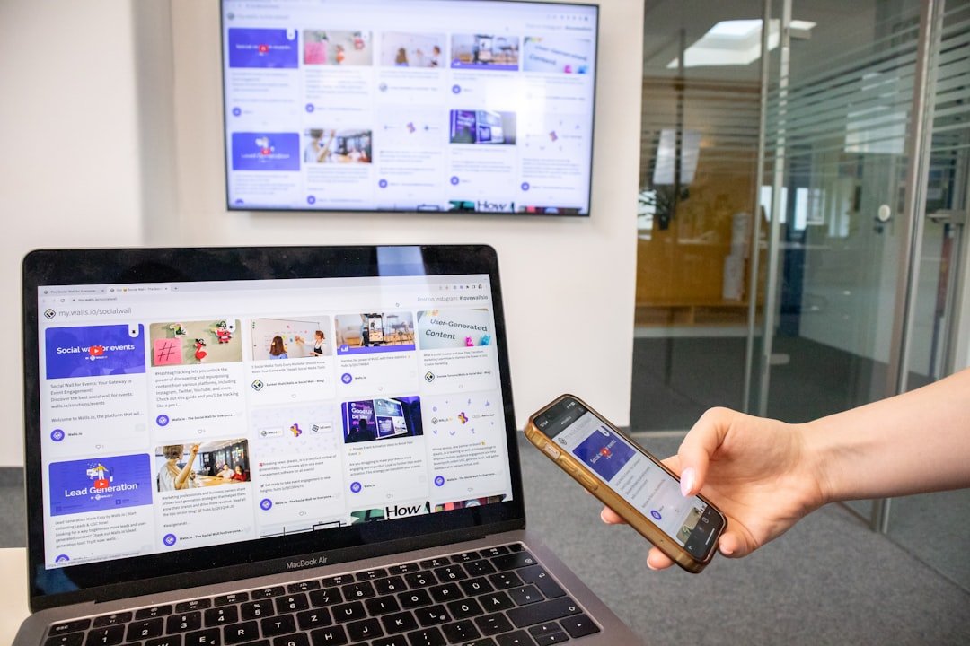 social-feed-img-04 A person holding a smartphone next to a laptop and a TV screen, showing a responsive website with a social wall embedded on it